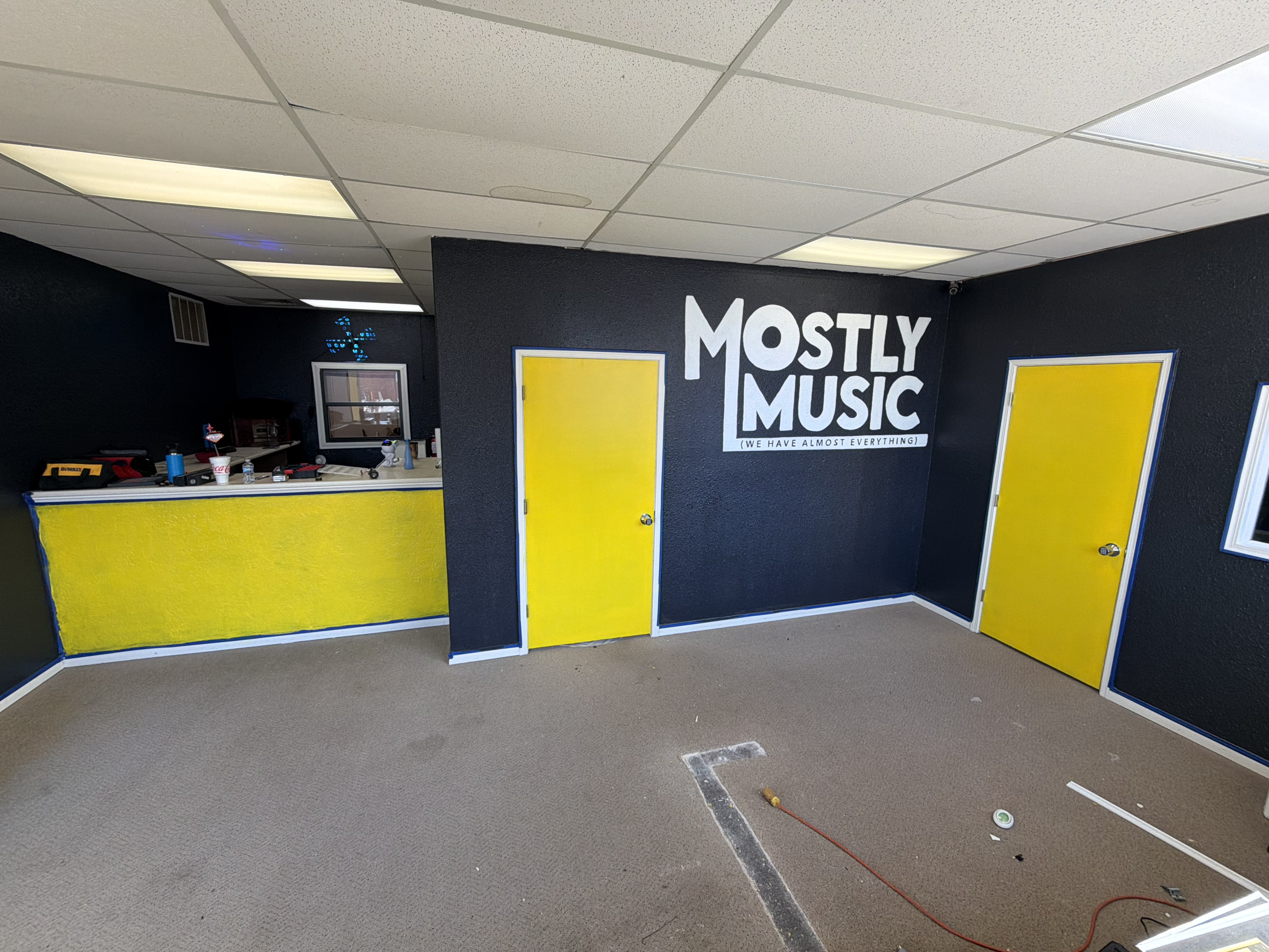 Inside the Mostly Music store in Pampa, TX — yellow service doors and the painted Mostly Music logo on a black wall