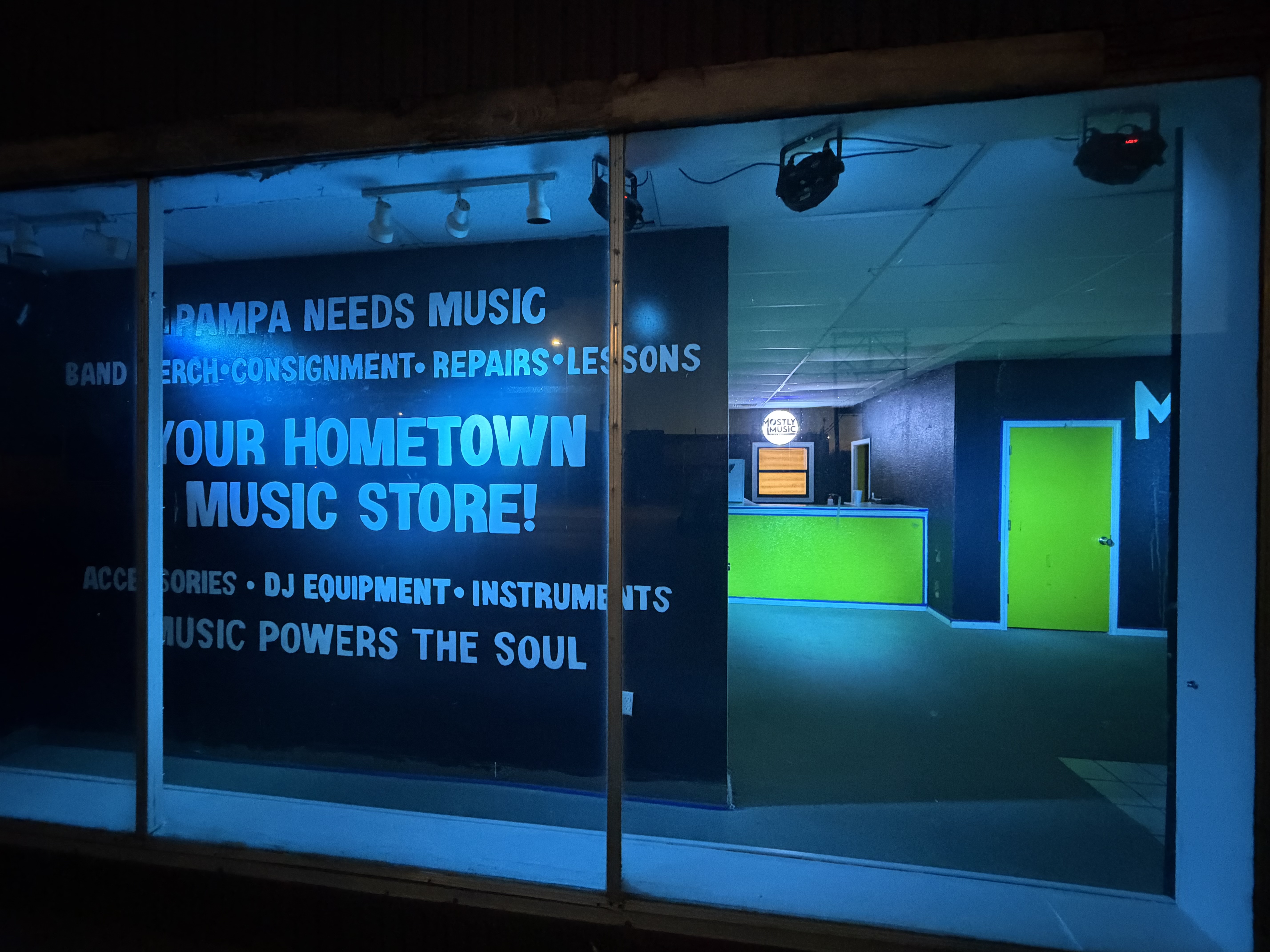 Mostly Music storefront window at night in Pampa, Texas — signage reads 'Pampa Needs Music — Your Hometown Music Store'